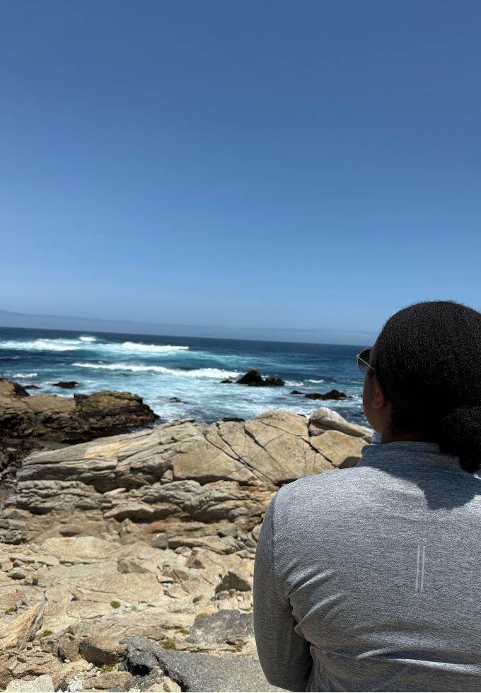 Mitchelle Matesva sits on rocks overlooking the ocean